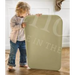 Leander Matty baby changing waterproof mat held upright by a child indoors on wood floor.