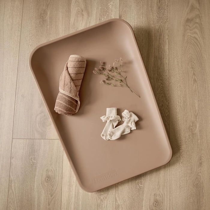 Leander Matty baby changing waterproof mat displayed on a wood floor with baby socks and towel.