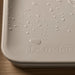 Leander Matty baby changing waterproof mat with water droplets on a wooden surface.