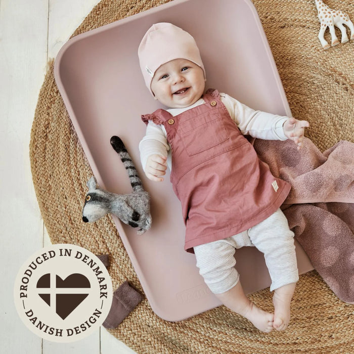 Leander Matty baby changing waterproof mat with smiling baby lying on it on woven rug.