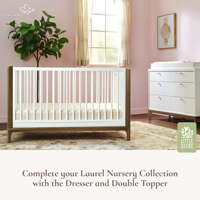 Little Seeds Laurel Island Convertible Crib in a nursery with pink walls, a dresser, and a potted plant.