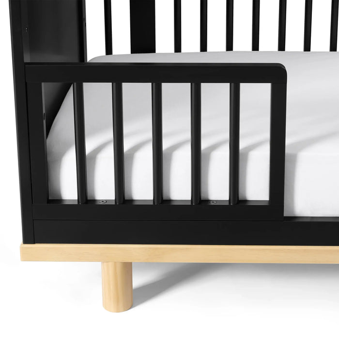 Little Seeds Spindle guardrail attached to a black crib with a white mattress and wooden base.