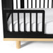 Little Seeds Spindle guardrail attached to a black crib with a white mattress and wooden base.