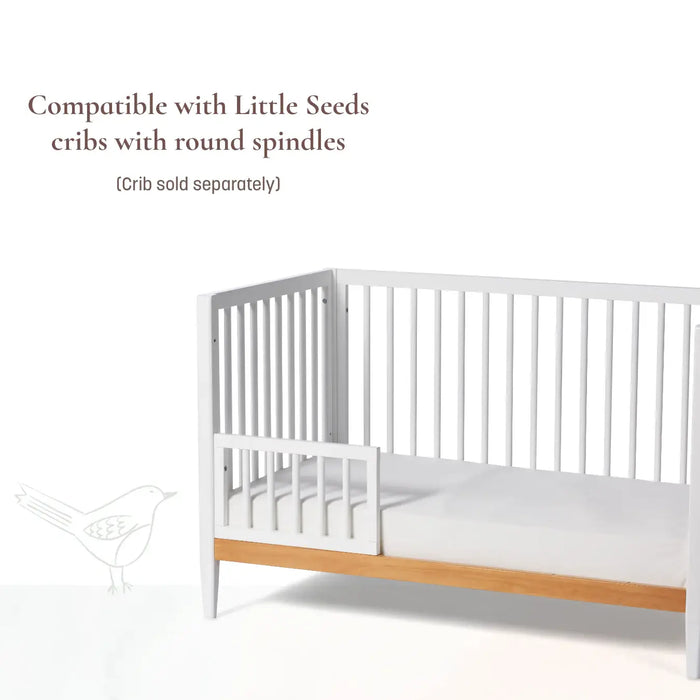 Little Seeds spindle guardrail shown attached to a white crib with round spindles on a white background.