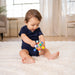 Manhattan Toy Atom Colorpop Rattle Teether held by a baby sitting on a white rug indoors.