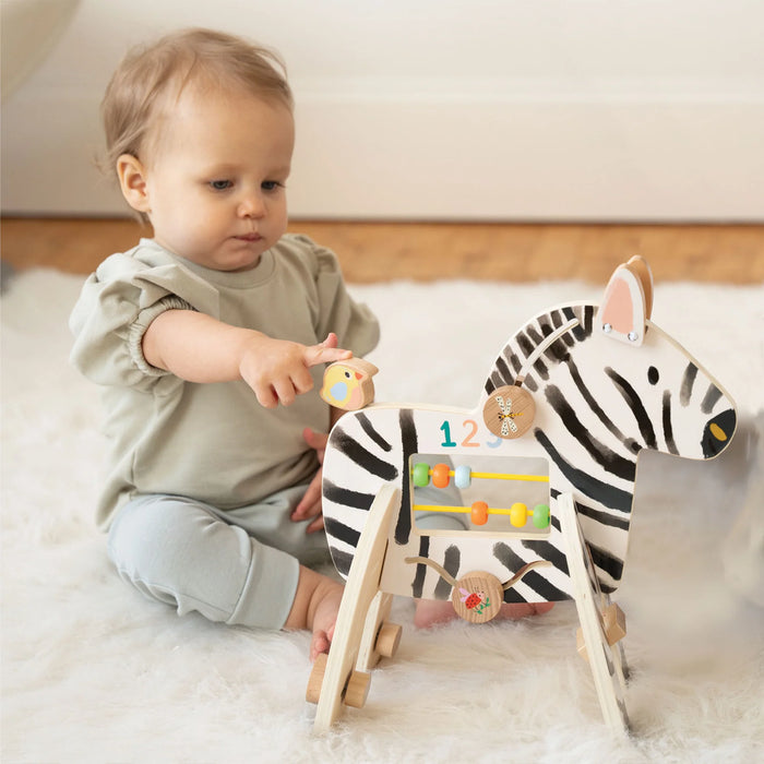 Manhattan Toy Safari Zebra wooden activity toy with a baby playing on a soft rug.