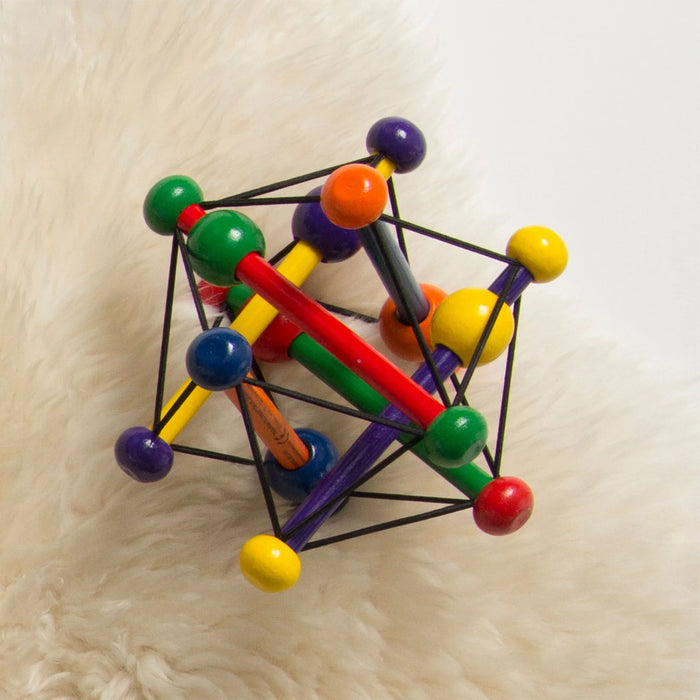 Manhattan Toy Skwish wooden rattle teether in bright colors resting on a soft cream surface.