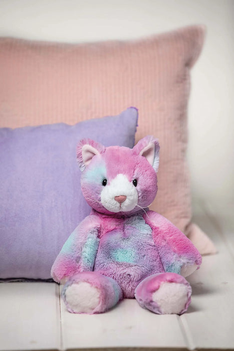 Mary Meyer Marchmello Zoo plush toy cat with pastel colors sitting on a bed with pink and purple pillows.