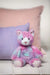 Mary Meyer Marchmello Zoo plush toy cat with pastel colors sitting on a bed with pink and purple pillows.