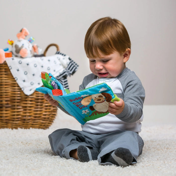 Mary Meyer Taggies Soft Book Teddy Dog held by a toddler sitting on a carpet.