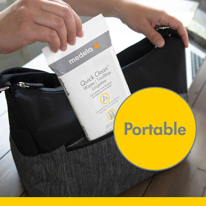 Medela Quick Clean breast pump wipes being placed into a diaper bag on a wooden table.