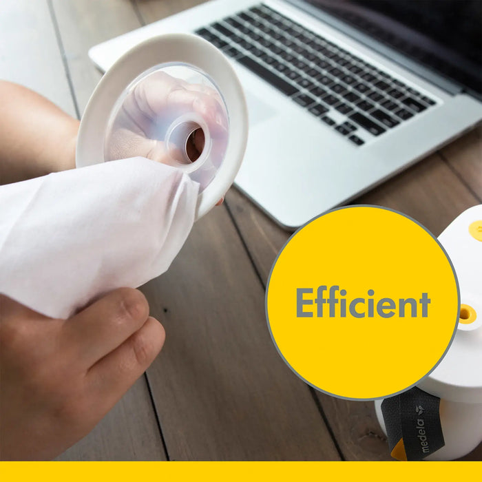 Medela Quick Clean breast pump wipe cleaning pump part on a wooden table near a laptop.