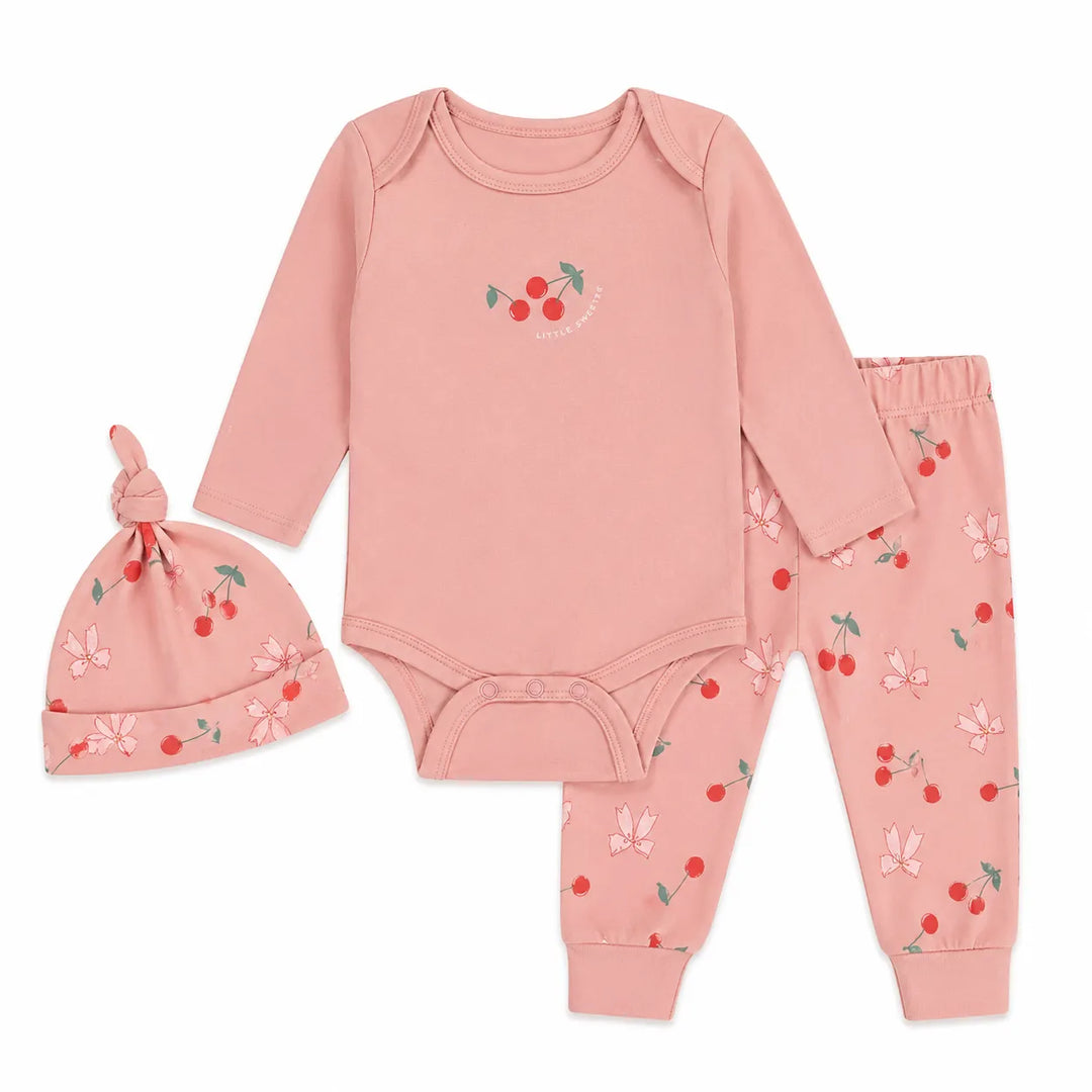 Three-piece baby set with cherry print, including pink bodysuit, pants, and matching hat, laid flat.