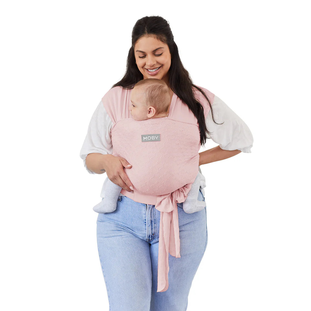 Moby Easy Wrap Baby Carrier in rose worn by woman carrying baby against white background.