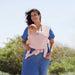Moby Easy Wrap baby carrier in rose pink shown worn by a woman carrying a baby outdoors.