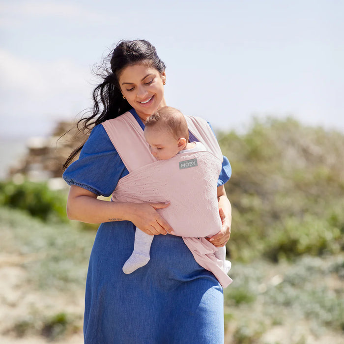 Moby Easy Wrap Baby Carrier Rose worn by a woman carrying a baby outdoors.