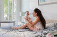 Mother sitting on a bed holding a smiling baby in a sunlit modern bedroom