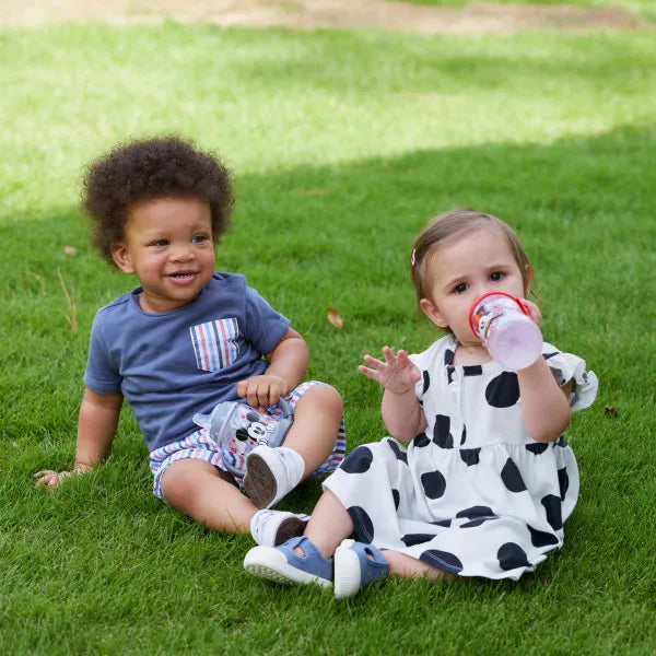 NUK Disney Mickey sippy cup for toddlers held by a child sitting on grass beside another toddler.