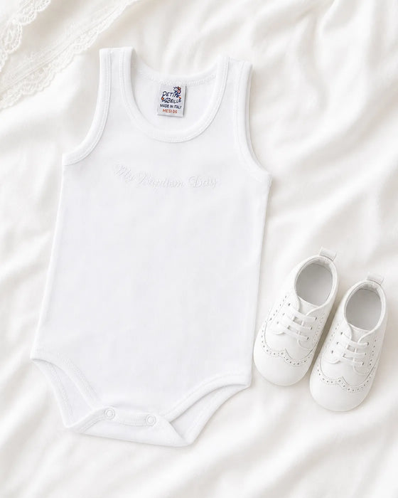 Petit Abeille baptism undershirt and white baby shoes displayed on soft white fabric.