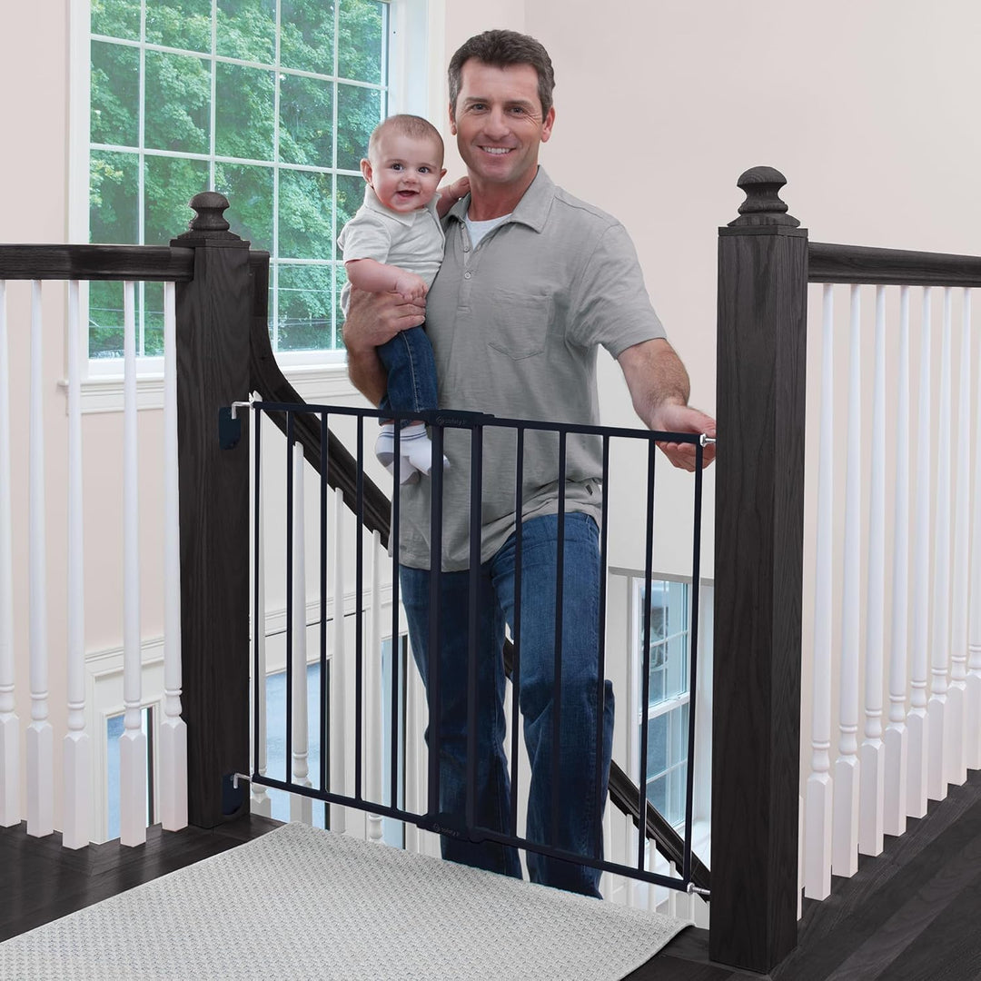 Man holding baby near black safety gate at top of staircase in home setting