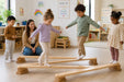 solid maple wooden balance board for kids - Children playing on a balance beam in a classroom setting with a teacher observing.