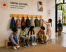 Children interacting with backpacks on the hard wood wall mount coat rack with hooks at a cultural center.