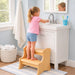 Child using a hard wood step stool to reach a sink in a bathroom