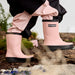 Stonz haze pink rain boots worn by a child outdoors on wood and rocks.