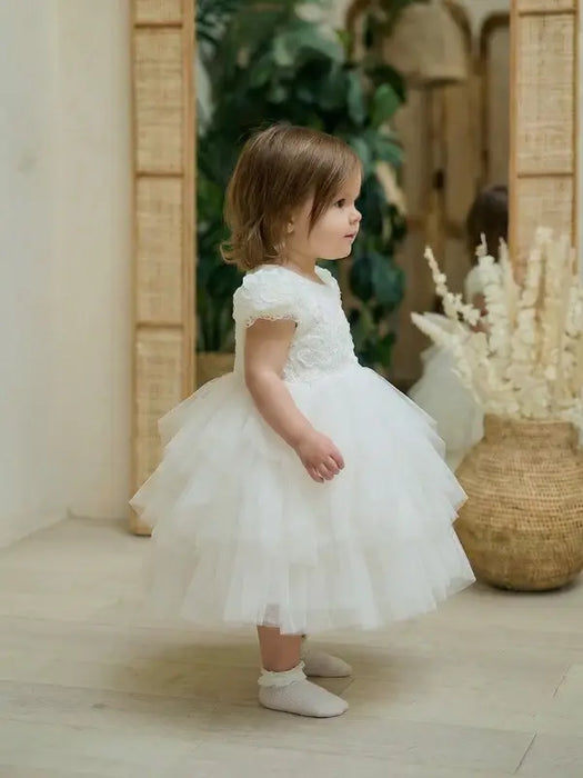 Warm Wendy off-white lace baptism dress shown on a toddler in an indoor setting with neutral decor.
