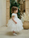 Warm Wendy off-white lace baptism dress shown on a toddler in an indoor setting with neutral decor.