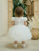 Warm Wendy off-white lace baptism dress shown on a toddler standing indoors facing a mirror.