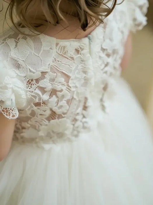 Warm Wendy off white lace baptism dress shown from the back on a young child indoors.