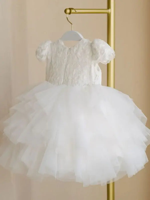 Warm Wendy off-white lace baptism dress with short sleeves and tulle skirt hanging on a gold rack