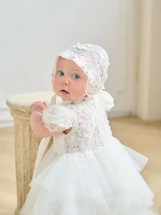 Warm Wendy off-white lace baptism dress shown on a baby standing indoors near a wooden stool.