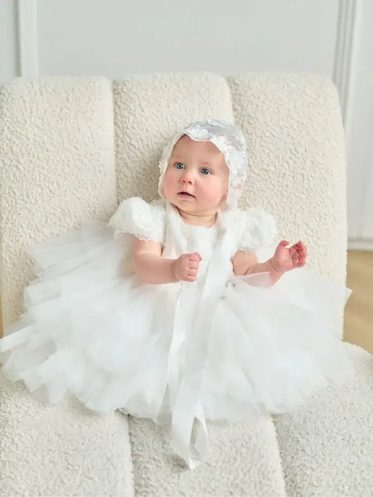 Warm Wendy Off-White Lace Baptism Dress shown on a baby sitting on a cream textured chair.