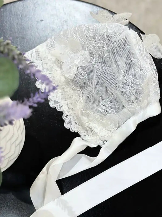 Teter Warm 3D floral detailing baby bonnet with lace and ribbon, displayed on a black surface.