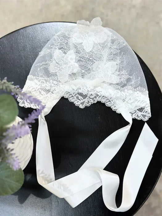 Teter Warm 3D floral lace baby bonnet with satin ties displayed on a black surface.