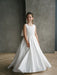 Teter Warm Tara satin bow communion dress worn by a young girl standing indoors on wood floor.