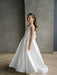 Teter Warm Tara satin bow communion dress worn by a girl standing indoors on a wooden floor.