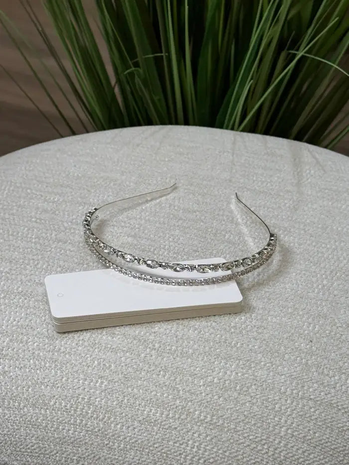Teter Warm Ace double band headpiece with crystals displayed on a textured table in front of green plants.