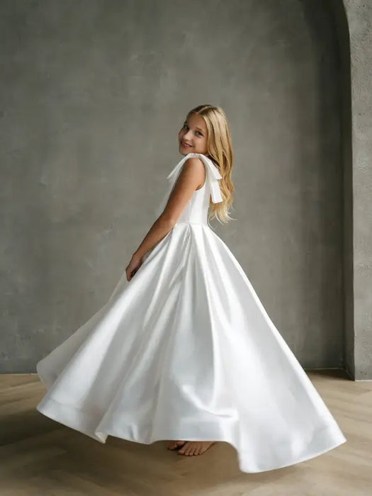 Teter Warm Addison satin bow shoulder communion dress worn by a smiling girl turning indoors.