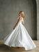 Teter Warm Addison satin bow shoulder communion dress worn by a smiling girl turning indoors.