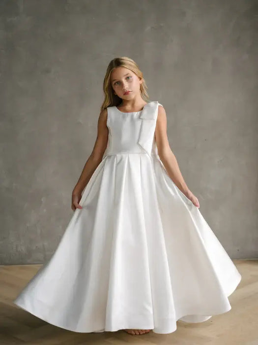 Addison satin bow shoulder communion dress on a young girl standing indoors against a gray backdrop.