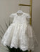 Teter Warm Adele off-white lace baptism dress displayed on a hanger in a softly lit room.