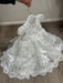 Teter Warm Adele off-white floral lace baptism dress on hanger, displayed indoors on wood floor.