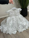 Teter Warm Adele off-white floral lace baptism dress on a hanger, shown indoors on wood floor.