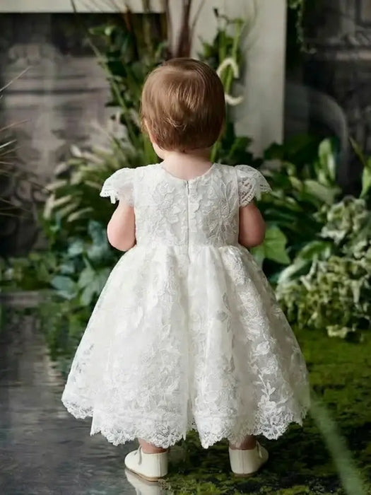 Teter Warm Adele off-white floral lace baptism dress shown on a toddler standing in a garden setting.