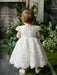 Teter Warm Adele off-white floral lace baptism dress shown on a toddler standing in a garden setting.