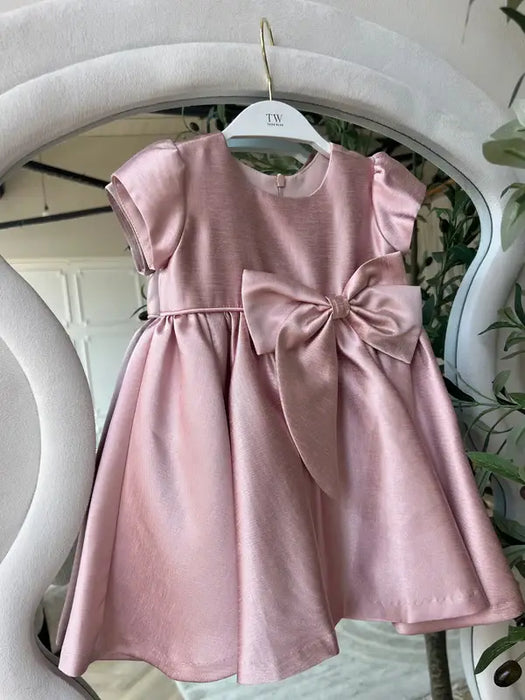 Teter Warm Ailani pink metallic party dress with short sleeves and large bow displayed on a hanger