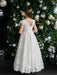 Angelica Lace Communion Dress shown on a girl standing in front of a decorated Christmas tree.